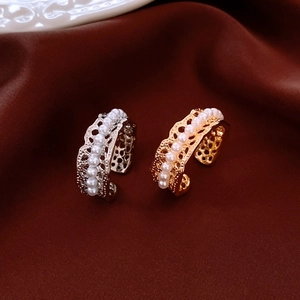 Close-up of elegant gold and silver hollow lace rings with pearls on dark satin cloth