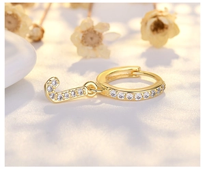 Macro shot of gold letter J hoop earring with micro-paved white zircons and dry flower decor