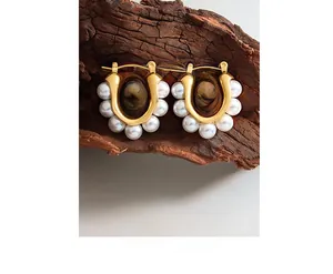 Macro view of gold plated U-shaped hoop earrings with white pearls on a rustic wood stand