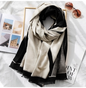 Detail of color-block scarf with geometric diamond patterns and soft tassels on white fabric