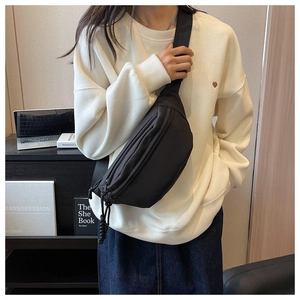 Detail view of a compact black canvas crossbody chest bag with woven zipper pulls
