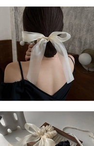 Detail of white she is cute ribbon bow hair clip and black elastic tie on wooden tray