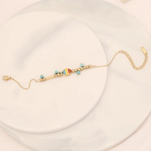 Detail of a gold stainless steel bracelet with blue beads and a colorful fish pendant