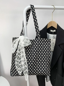 Detailed view of the black polka dot tote bag featuring a large white lace bow accent