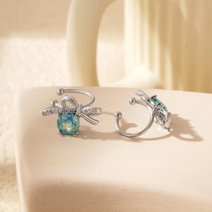 Silver bow ear clips with blue faceted stones and diamond accents on beige background