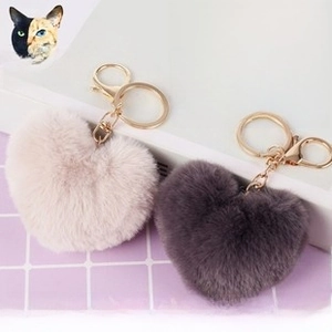 Detail of pink and purple heart-shaped fluffy pompom keychains with gold lobster clasps
