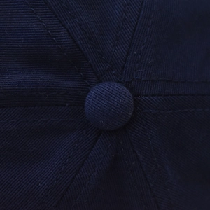 Close-up of the top button and stitched seams on a navy blue washed cotton baseball cap