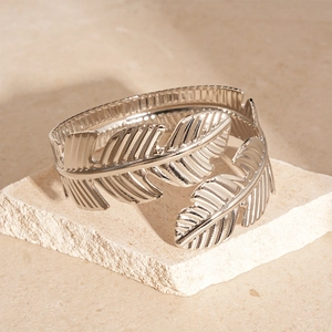 Detailed view of silver leaf-textured open metal bracelet on stone pedestal