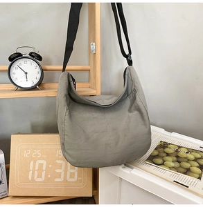Detail of grey nylon crossbody bag hanging on a wooden rack in a minimalist room