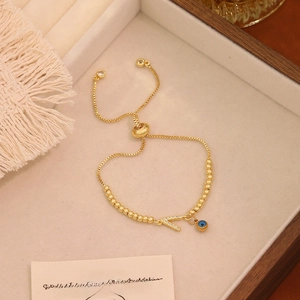 Dettaglio del bracciale a sfere dorate con lettera V in cristallo e ciondolo occhio blu