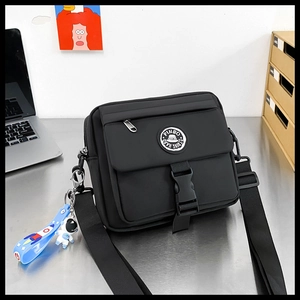 Close-up of black nylon messenger bag with buckle closure and astronaut keychain accessory