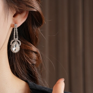 Close-up of sparkling teardrop earrings with halo diamonds on a model for luxury style