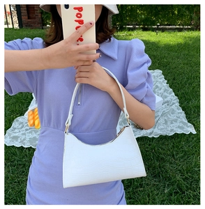 Close-up of white crocodile pattern shoulder bag held by model in outdoor natural setting
