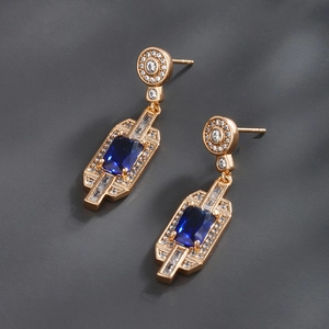 Detailed macro view of gold earrings featuring rectangular blue gems and white cubic zirconia