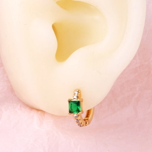 Detail of gold hoop earring featuring an emerald-cut green stone on a model ear