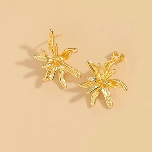 Macro shot of gold irregular floral earrings with polished metallic surface on beige