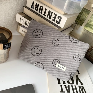 Detailed view of grey corduroy makeup bag with black smiley patterns on a minimalist desk