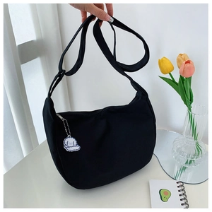 Detail of black canvas crescent hobo bag with a cute white puppy pendant and adjustable strap