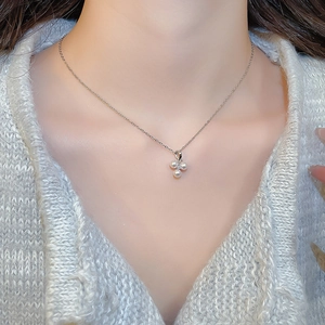 Detail of stainless steel necklace featuring a zircon and triple pearl pendant on grey knitwear