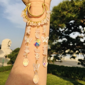 Outdoor view of golden dreamcatcher earring with pink crystals and butterfly charms