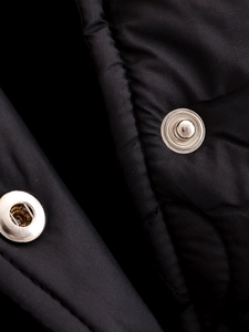 Detail of black quilted puffer jacket featuring glossy fabric and silver metal snap buttons