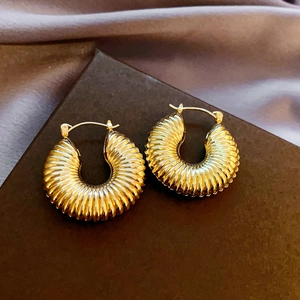 Close-up of golden ribbed hoop earrings on elegant purple silk background fabric