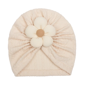Macro detail of beige knitted baby hat featuring a 3D floral decoration on soft fabric