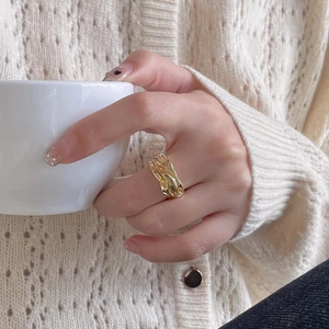 Detailed view of a gold irregular lava texture ring worn by a model in a cozy setting