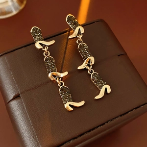 Detailed view of gold tassel earrings with rhinestone stiletto heels on leather