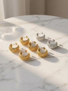 Detail of C-shaped hoop earrings featuring gold and silver woven texture on marble