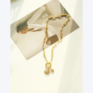 Gold paperclip chain necklace with Hamsa and sun pendants on an aesthetic magazine background