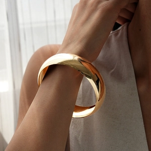 Close-up of minimalist chunky golden round bangle worn on wrist with elegant lighting