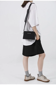 Side view of a black minimalist crossbody bag with silver logo worn by a model