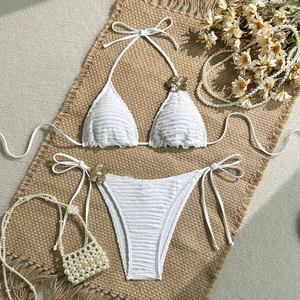 Detail of white bikini set with gold floral charms and textured pleated fabric on straw mat