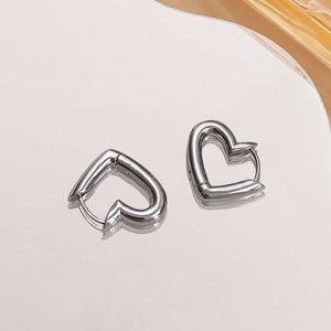 Close-up of heart-shaped silver earrings with a polished mirror finish on gray surface