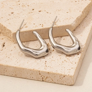 Close-up of irregular C-shaped 304 stainless steel earrings on beige stone slabs