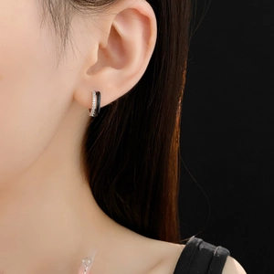 Macro shot of silver and black geometric hoop earring with zircon on a model's ear