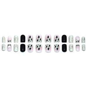 Short press-on nails with black cow print, white hearts, and pearls on a white background