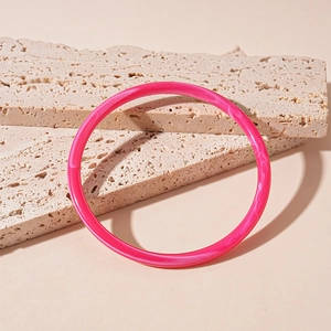 Détail d'un bracelet en acrylique rose avec texture ondulations sur fond de pierre