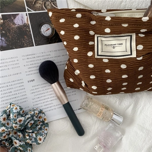 Detailed view of a brown pleated polka dot makeup bag styled with beauty accessories
