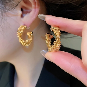 Detailed close-up of gold-plated twisted C-shaped stud earrings showing metallic spiral texture
