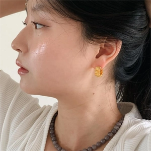 Close-up of textured golden C-shape hoop earrings worn by a model in a minimalist style