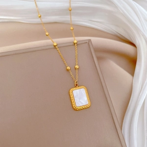 Detail of gold titanium necklace with square shell pendant and twisted edge on silk background