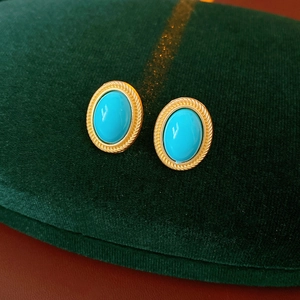 Close-up of vintage oval blue turquoise earrings with golden braided frames on velvet