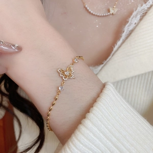 Detail of an 18k gold plated bracelet with a zircon butterfly charm on a model's wrist