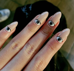 Close-up of nude oval nails featuring unique black and white evil eye patterns at the base