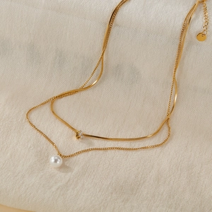 Close-up of double-layer gold necklace with flat snake chain, pearl and zircon detail