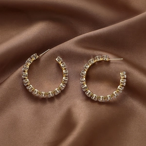 Detail of gold C-shaped hoop earrings with sparkling cubic zirconia on brown silk fabric