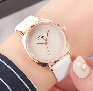 Close-up of a stylish square gold watch with a white leather strap on a female wrist