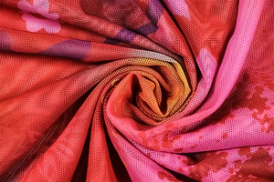 Macro shot of breathable mesh fabric with vibrant pink and red tie-dye print patterns